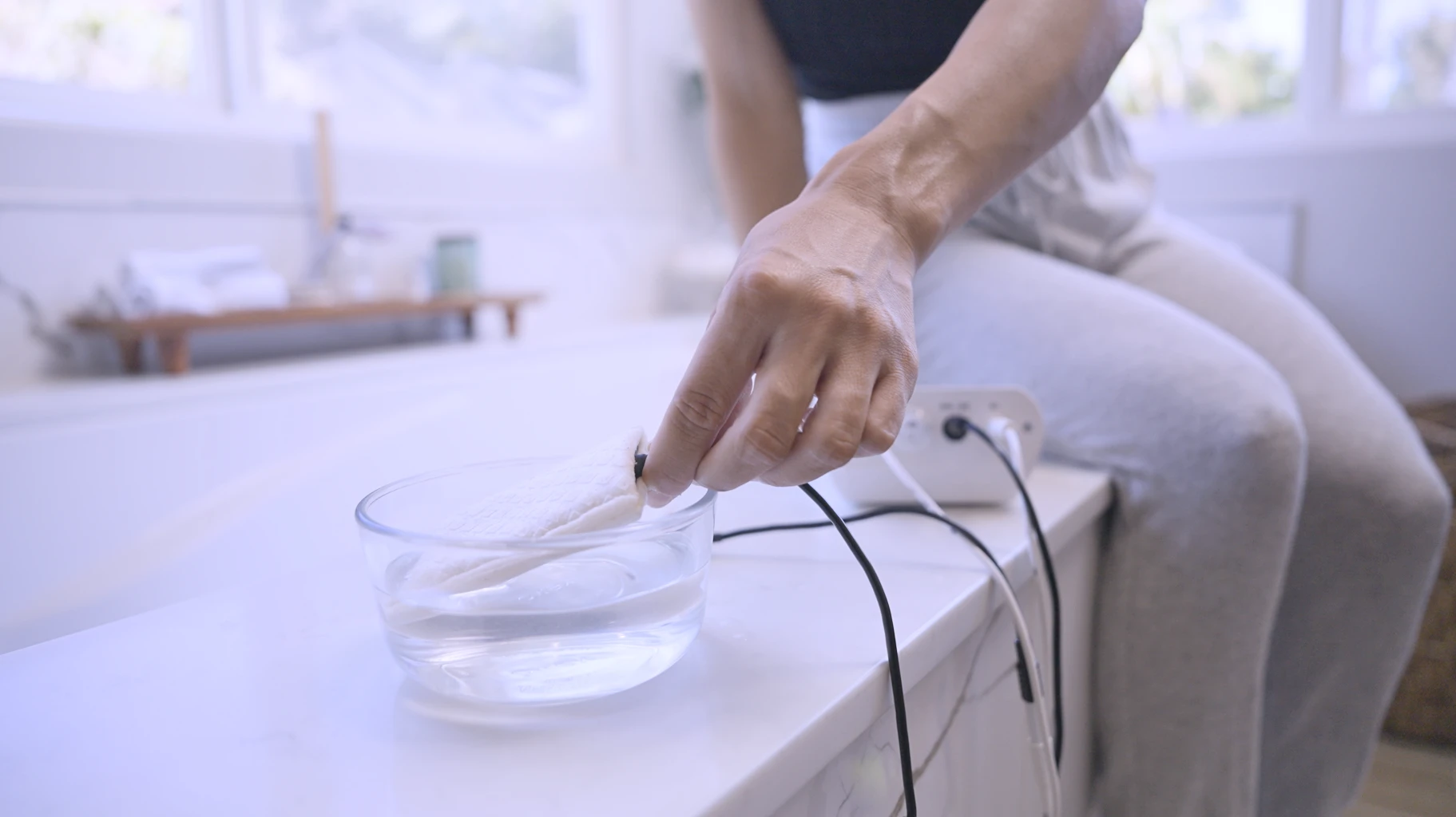 Image: Captured in this photograph, a woman is seen immersing one of the underarm attachments of the Fischer iontophoresis device into a cup of water, employing it to manage her axillary hyperhidrosis, marked by excessive underarm sweating. This innovative solution is provided by RA Fischer Co. through their original metal-free iontophoresis device, "The Fischer," designed with precision to tackle hyperhidrosis effectively.