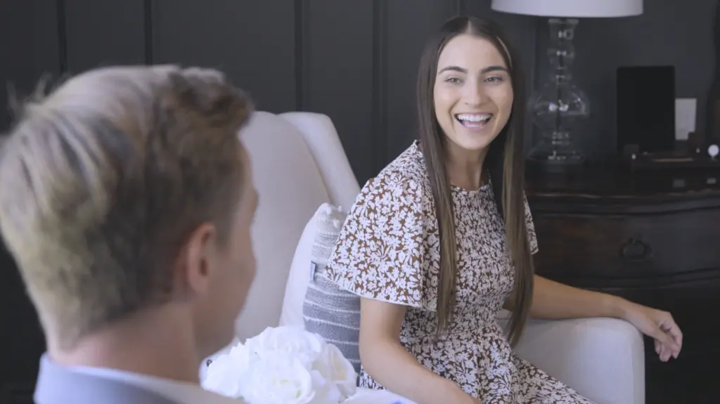 In a comfortable living room scenario, a woman with brown hair sits on a white couch, engrossed in a conversation with a man who shares the cozy ambiance. She is elegantly dressed in brown attire. Concurrently, she effectively manages her plantar hyperhidrosis, characterized by excessive foot sweating, using RA Fischer Co.'s original metal-free iontophoresis device, "The Fischer." This specialized device is meticulously tailored to tackle hyperhidrosis, offering a comprehensive solution for her condition.