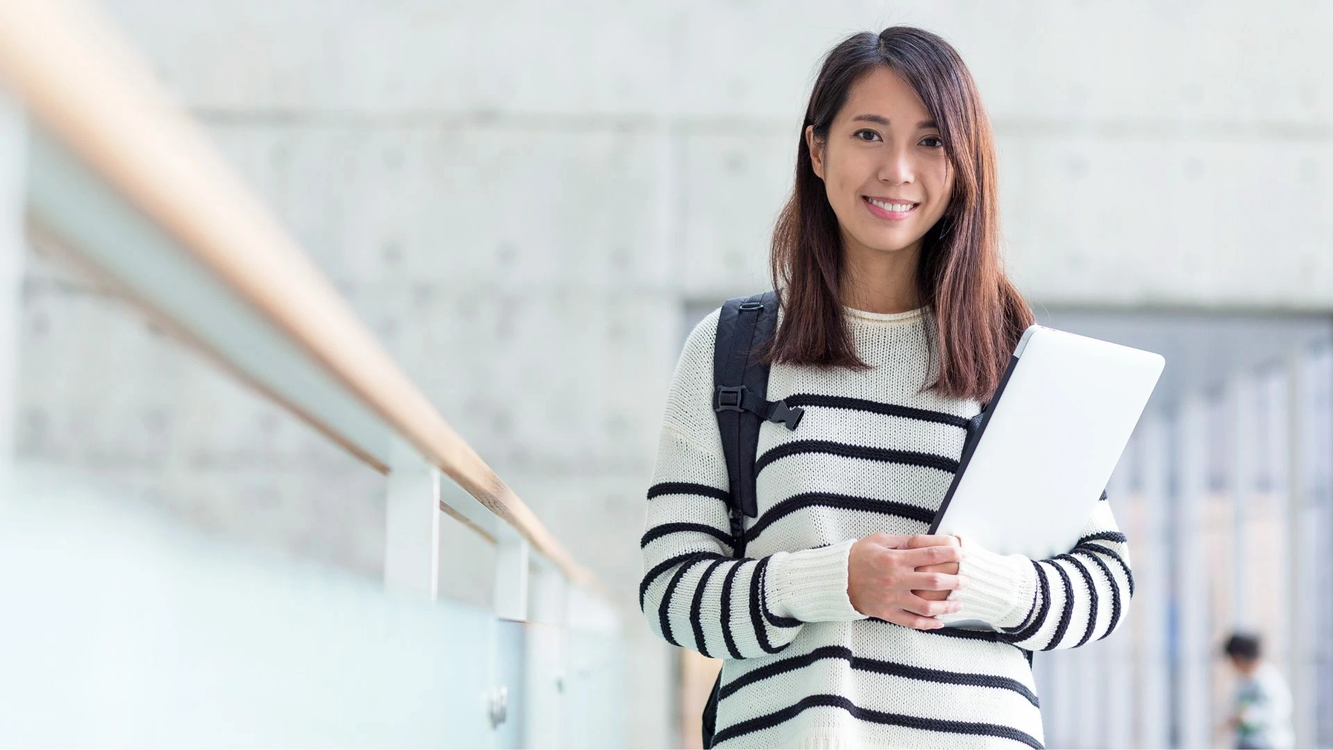 Picture of a student and patient from RA Fischer. She is smiling, wearing a striped sweater, backpack, and holding a laptop [ contact RA Fischer treatment specialists ]